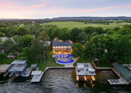 Wide drone view of lakefront home, pool, and Hill Country countryside at dusk