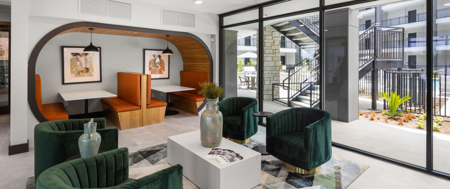 Modern apartment lounge with arched wood nook, emerald green velvet chairs and courtyard view by Boko Media