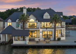 Twilight waterfront home with boat dock, palm trees, and lit balconies