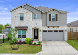 Two-story stone home with balcony, garage, and manicured lawn