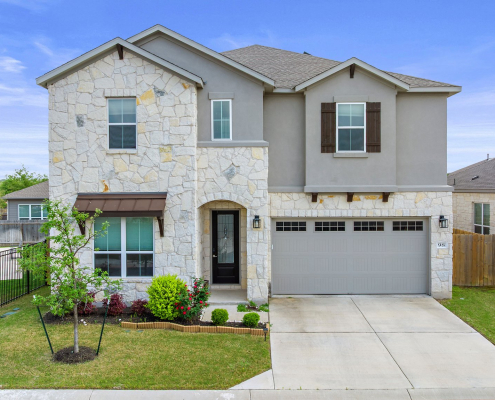Two-story stone home with balcony, garage, and manicured lawn